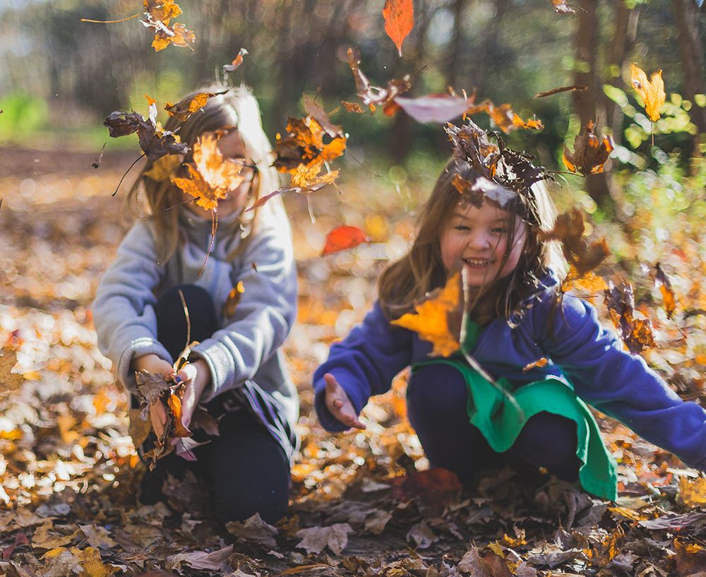 niñas jugando con las ojas de árboles en otoño sonriendo